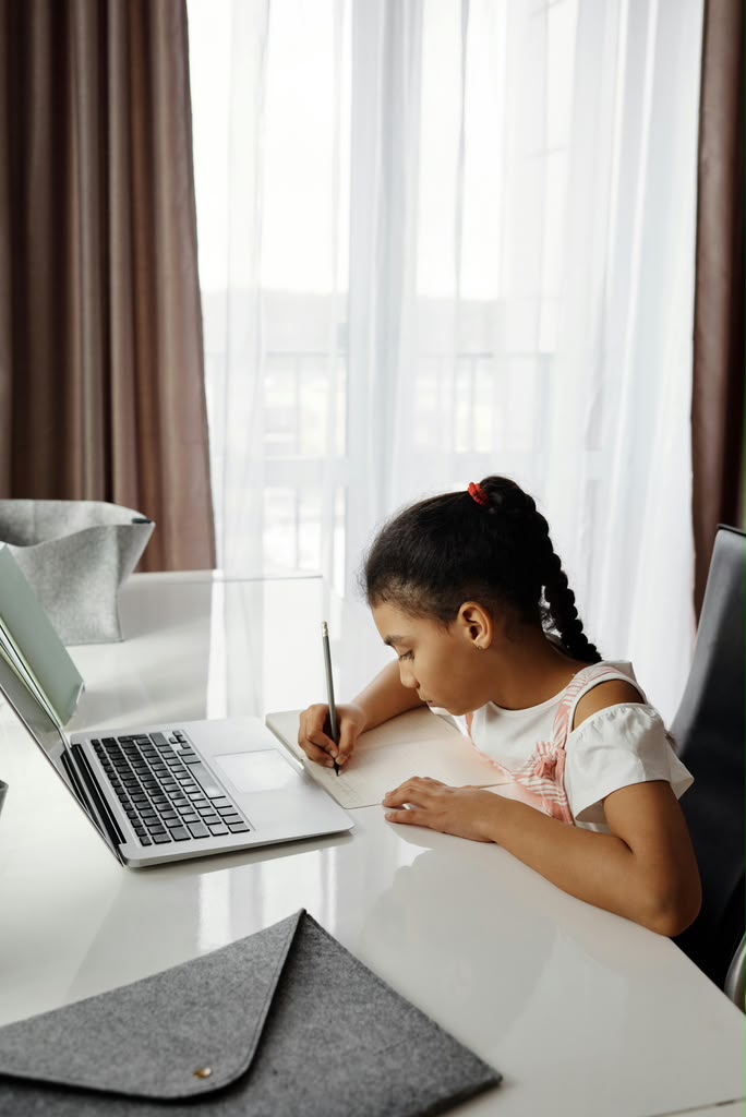 Girl writing in her notebook beside a laptop